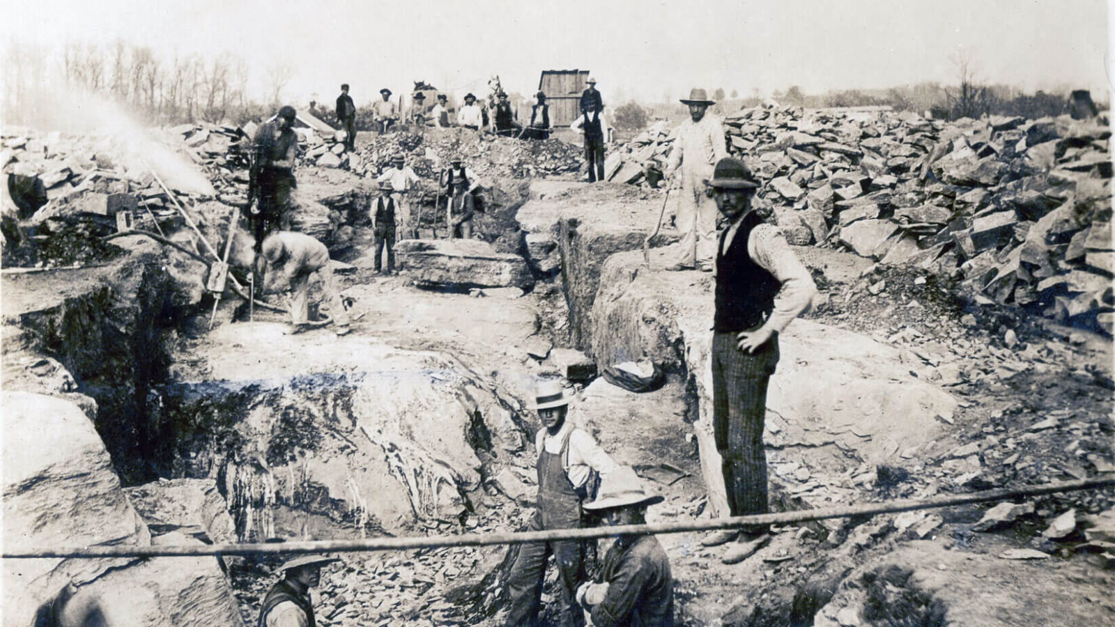 Workers use shovels and a jackhammer to dig the foundation.